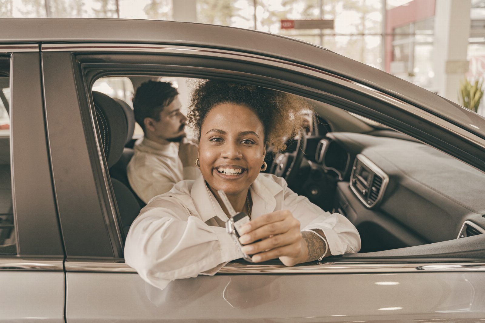 Joyful couple in their new car, holding keys in a dealership showroom, smiling warmly.