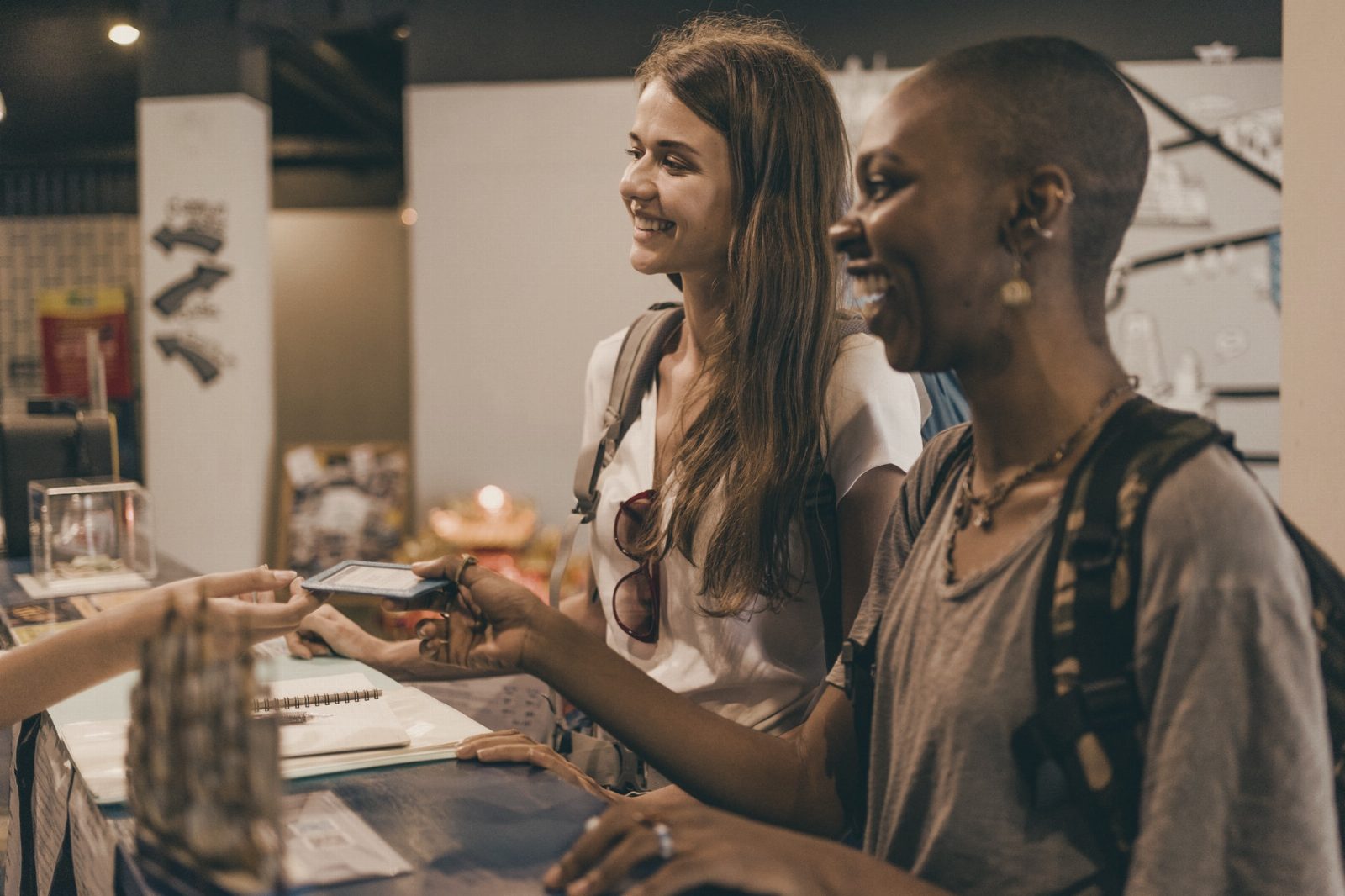 Two women enjoying a cheerful check-in at a hostel reception desk.