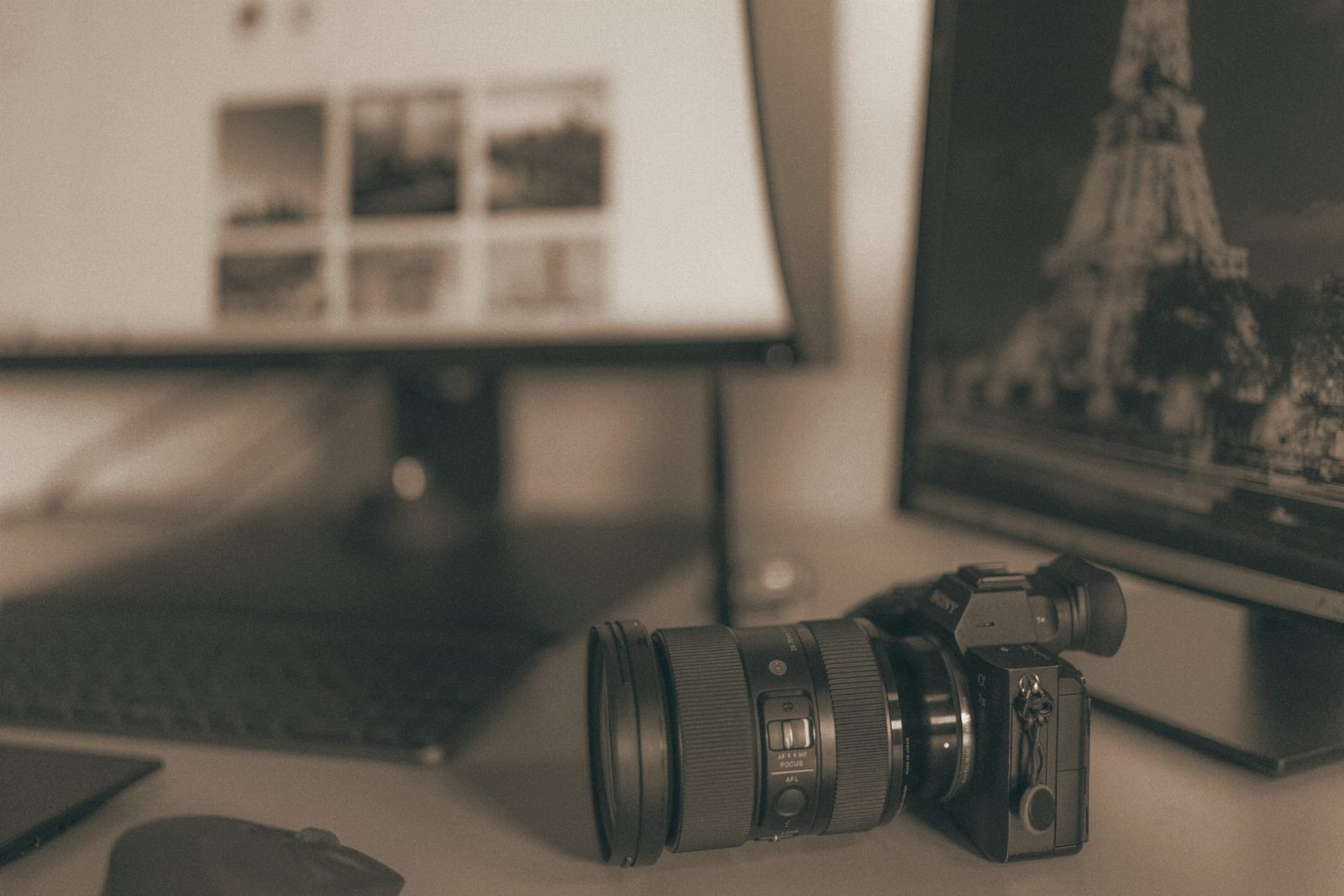 Black and white image of a desk with SLR camera and monitors, ideal for technology themes.