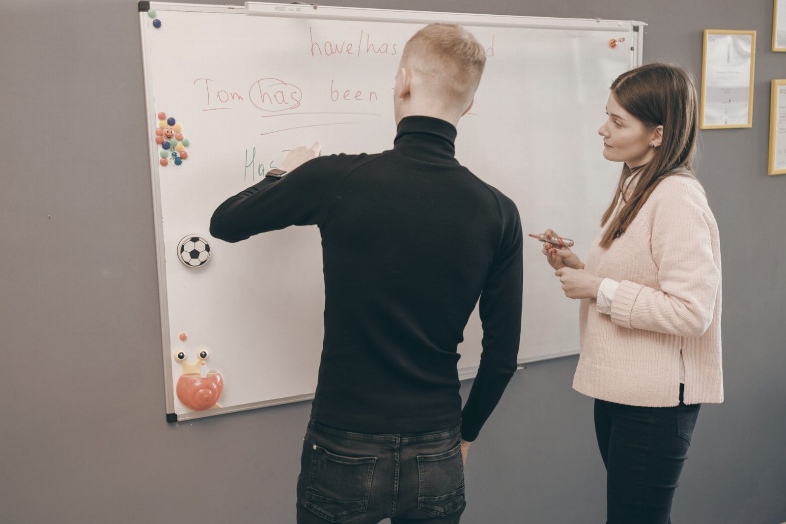 A student and teacher engage in an English lesson on a whiteboard. Indoor educational setting.