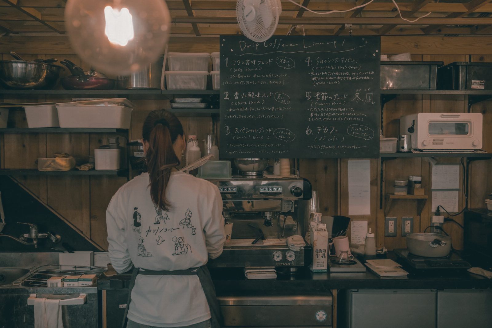 Barista making coffee in a warm, rustic cafe with a detailed menu chalkboard.
