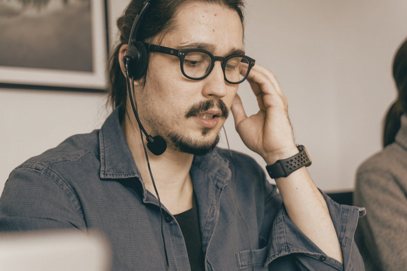 A bearded man with glasses and headphones working in a call center, providing customer support.
