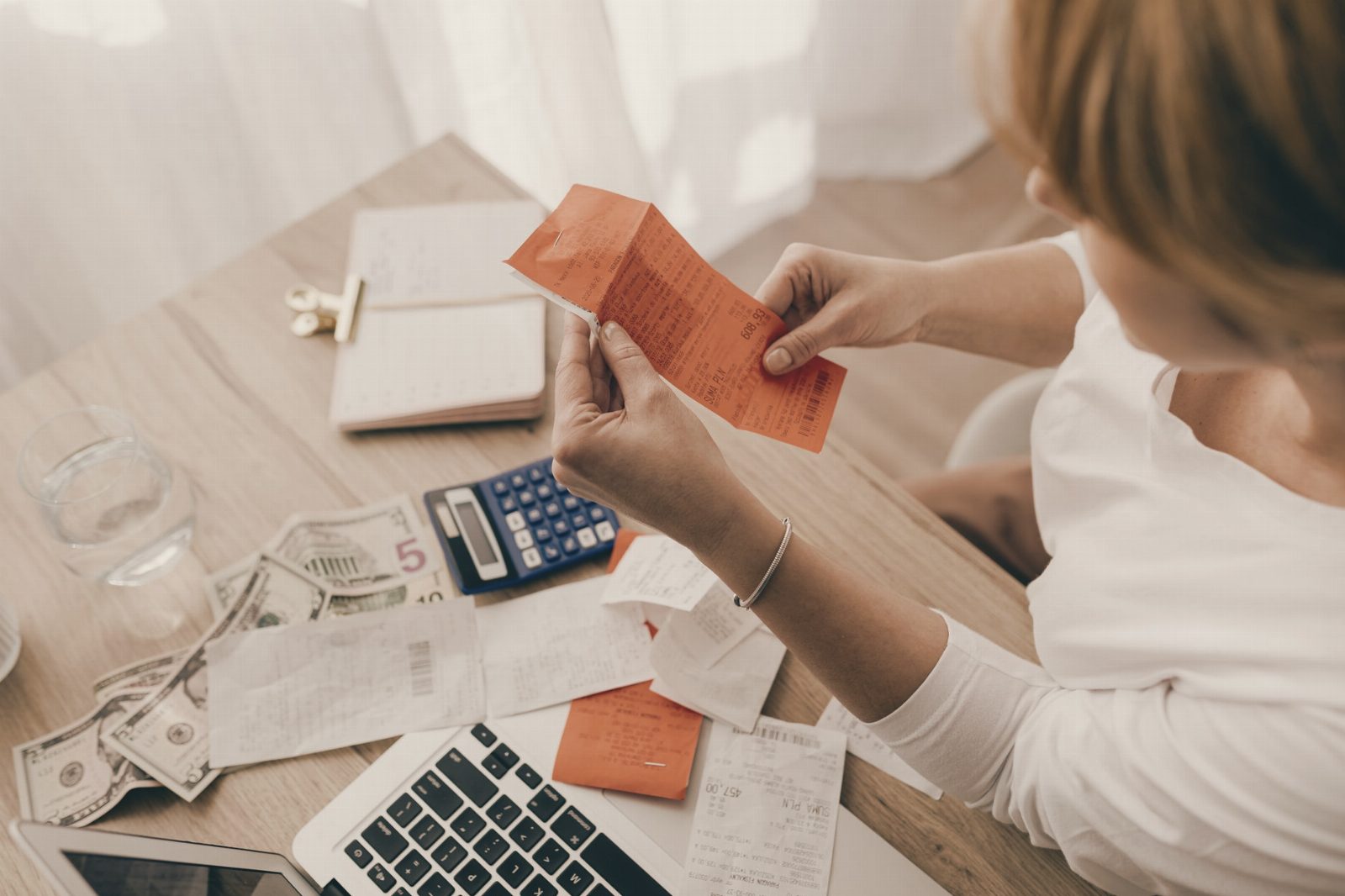 Woman using calculator and receipts at home office desk for finance management.