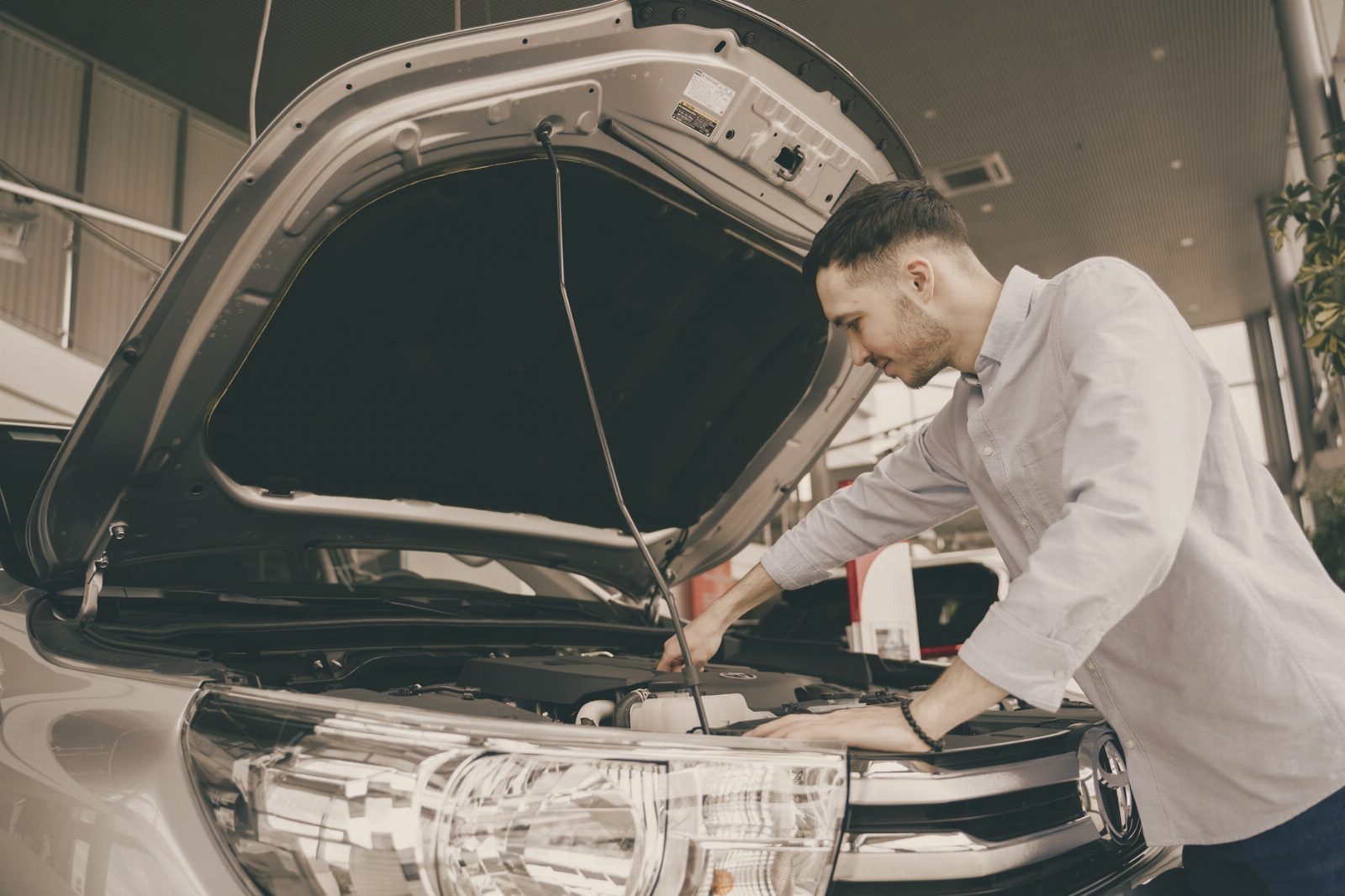 A man in a blue shirt examines a car's engine in a modern vehicle showroom.