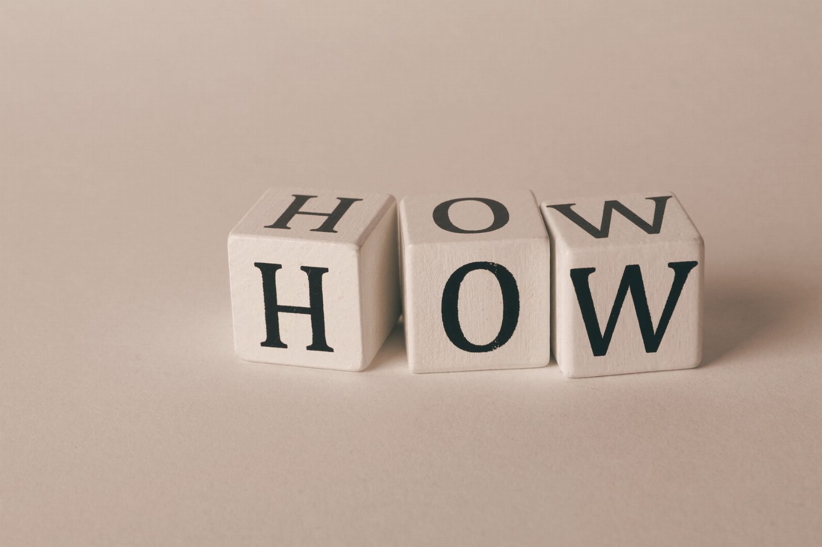 Close-up of white wooden cubes with the letters 'H', 'O', and 'W' arranged on a neutral background.