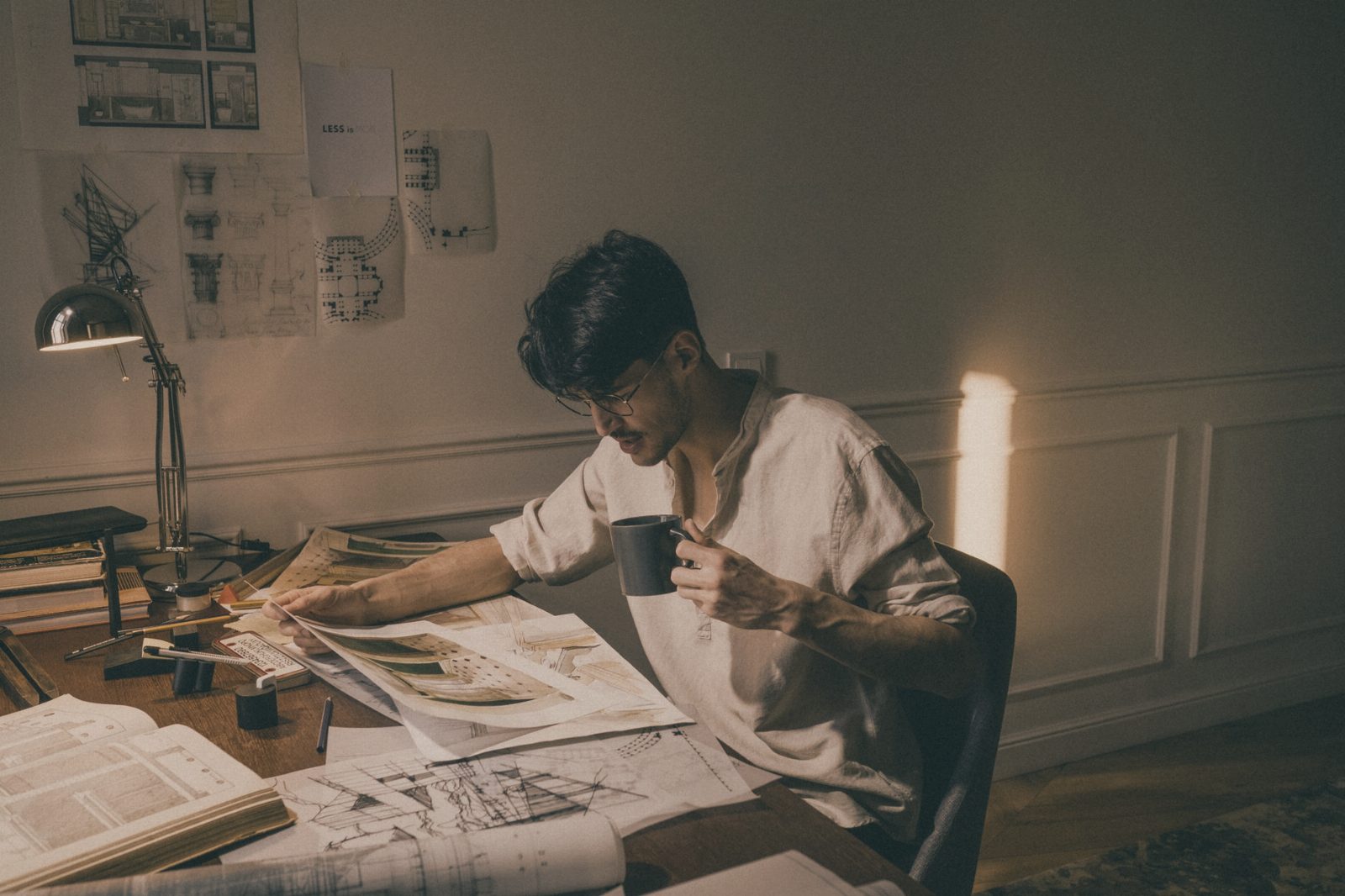 A creative architect working at home, reviewing blueprints with coffee.