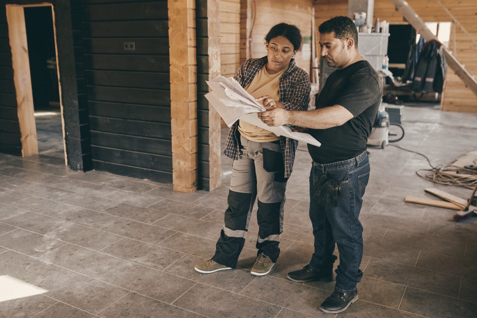 Two workers examining blueprints inside a building under construction, showcasing teamwork.
